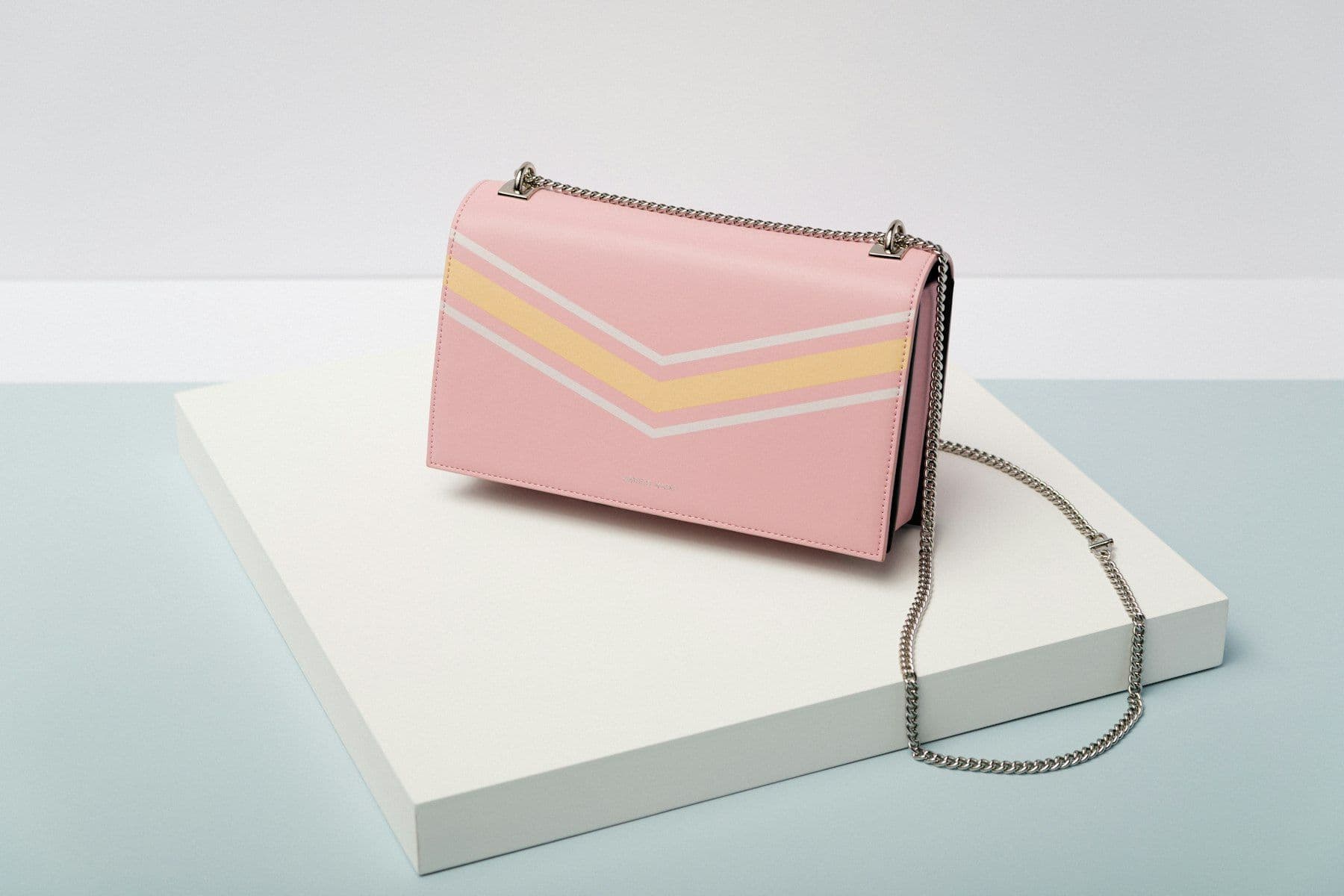 Pale pink shoulder bag with a chain strap on a white plinth